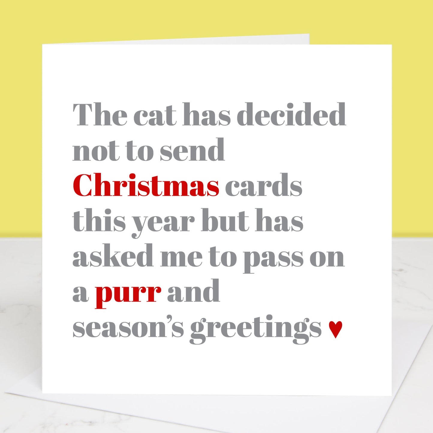 A Christmas card with a white background featuring text that mimics a cat's decision not to send Christmas cards. The card is blank and has a yellow background behind it.