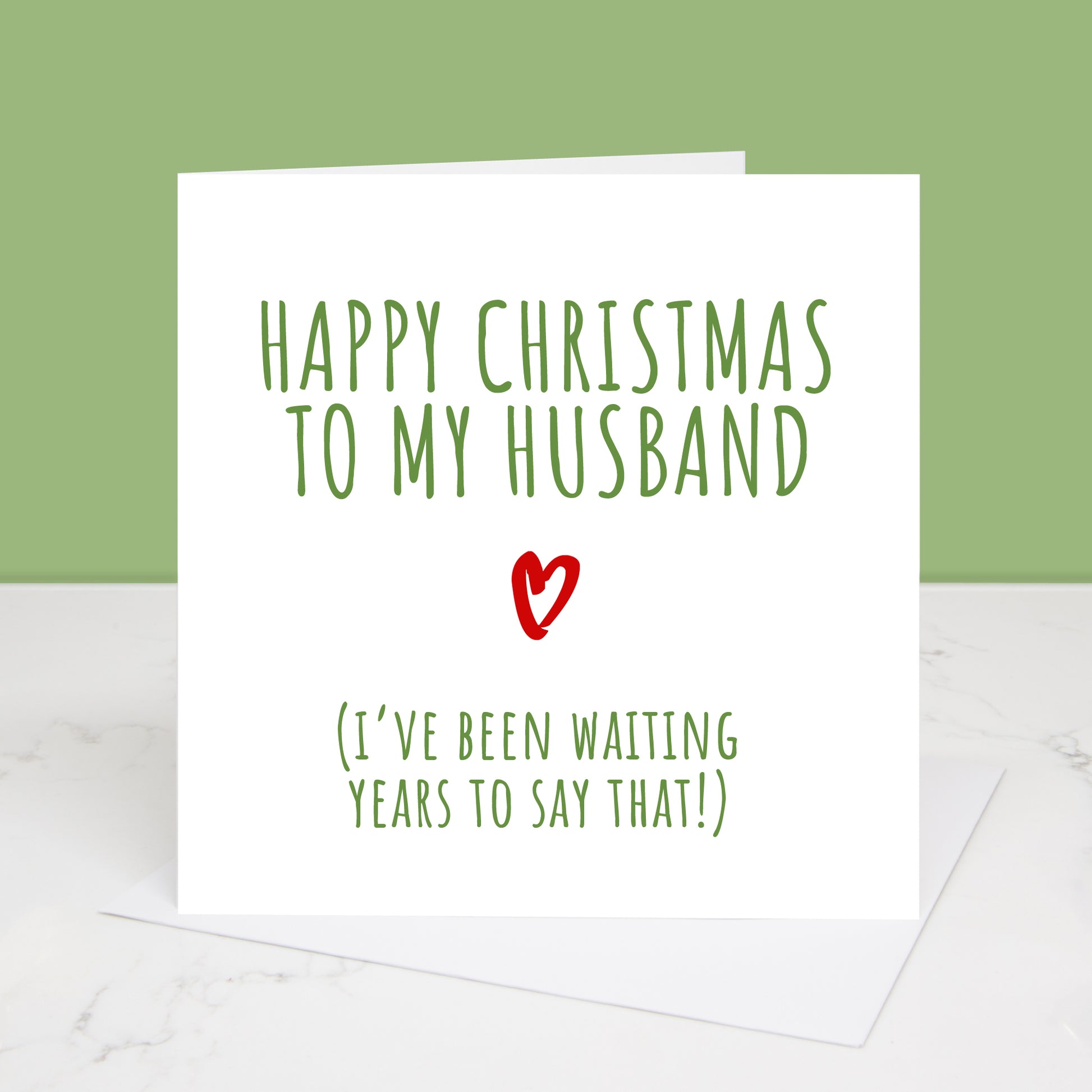A Christmas card with green and red text that reads 'Happy Christmas to my Husband (I've been waiting years to say that!)' with a heart symbol.