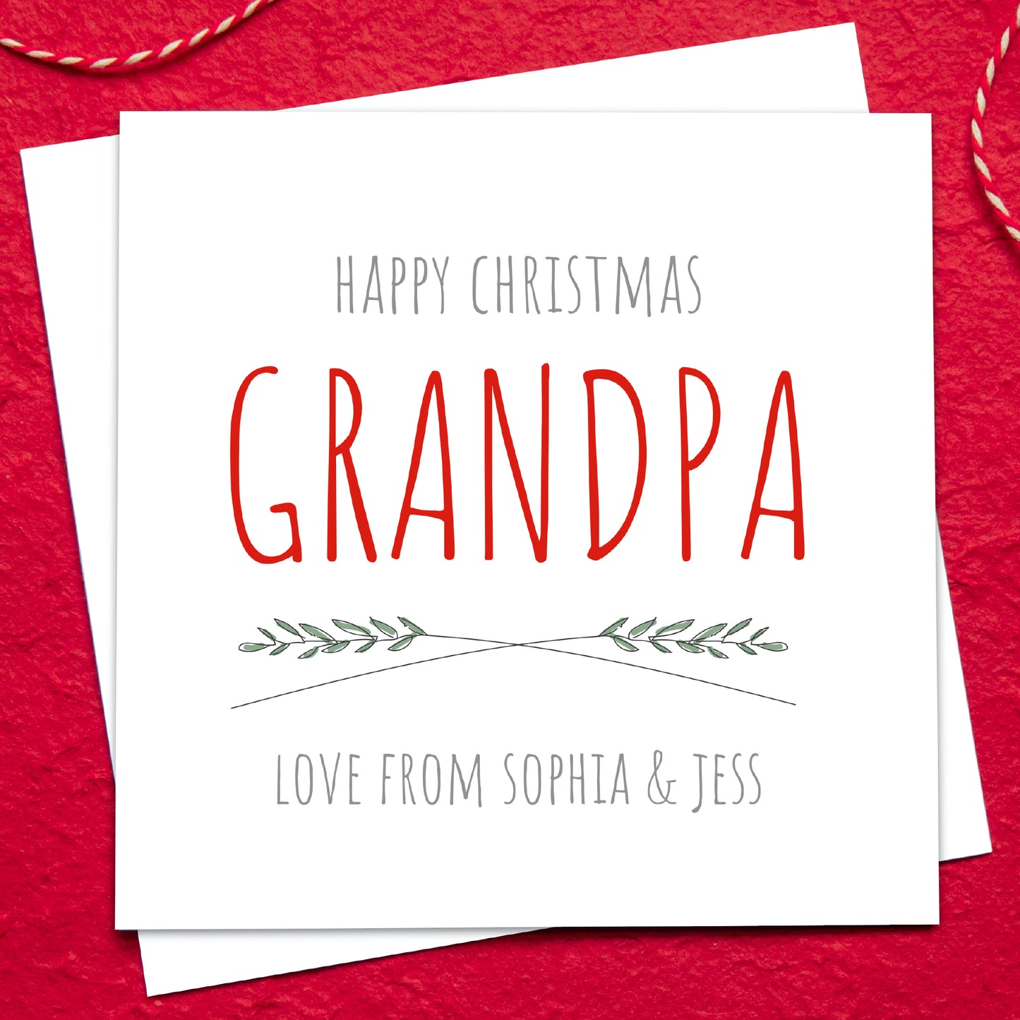 Christmas card for Grandpa with red text on a white background, placed on a red textured surface.
