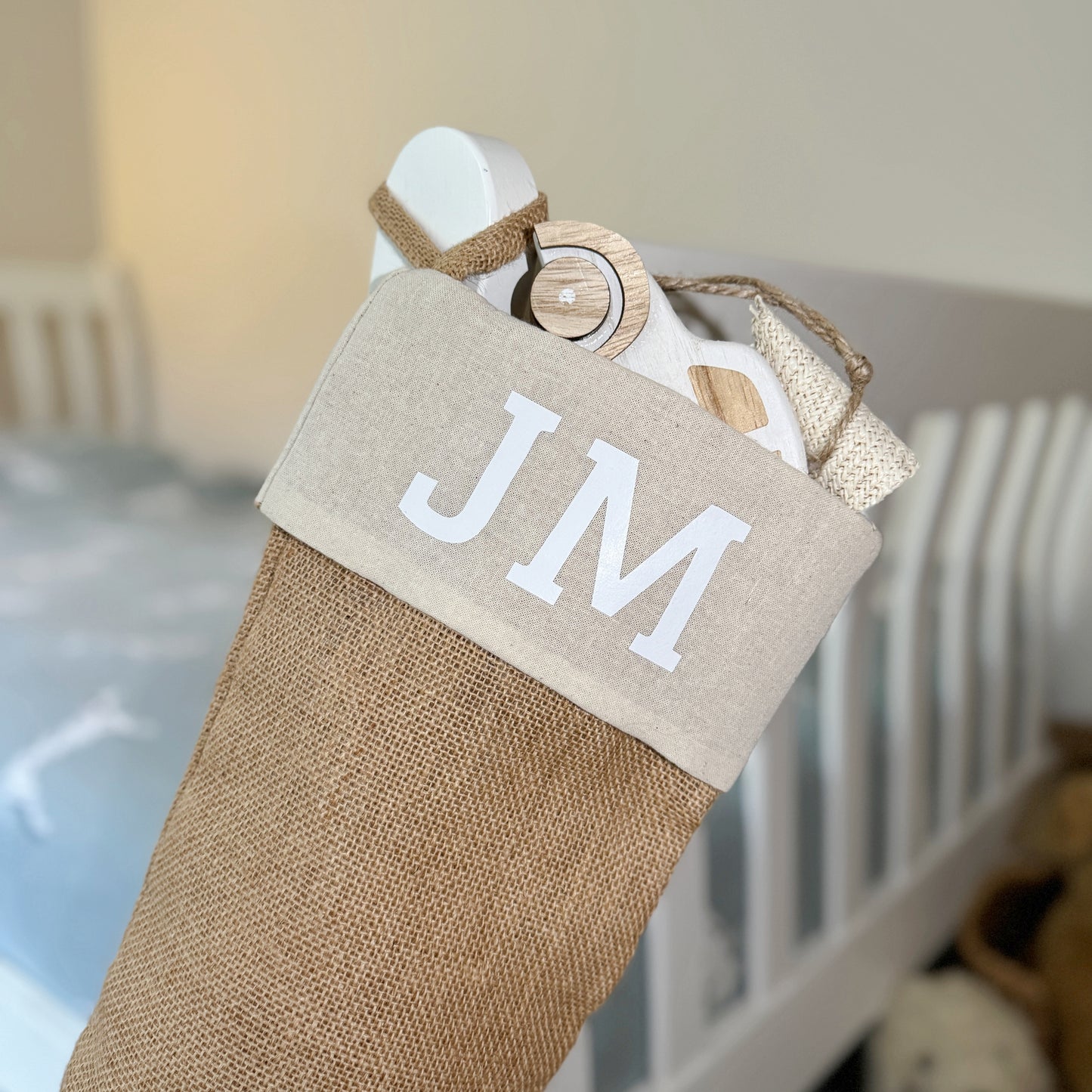 Burlap Christmas stocking with 'JM' initials hanging on a bedstead.