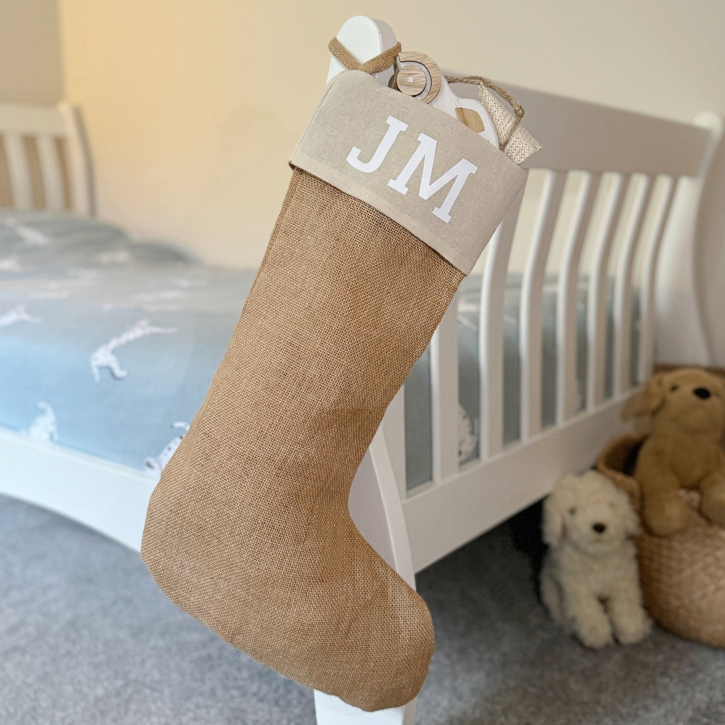 Jute Christmas stocking with 'JM' initials hanging on a bed.