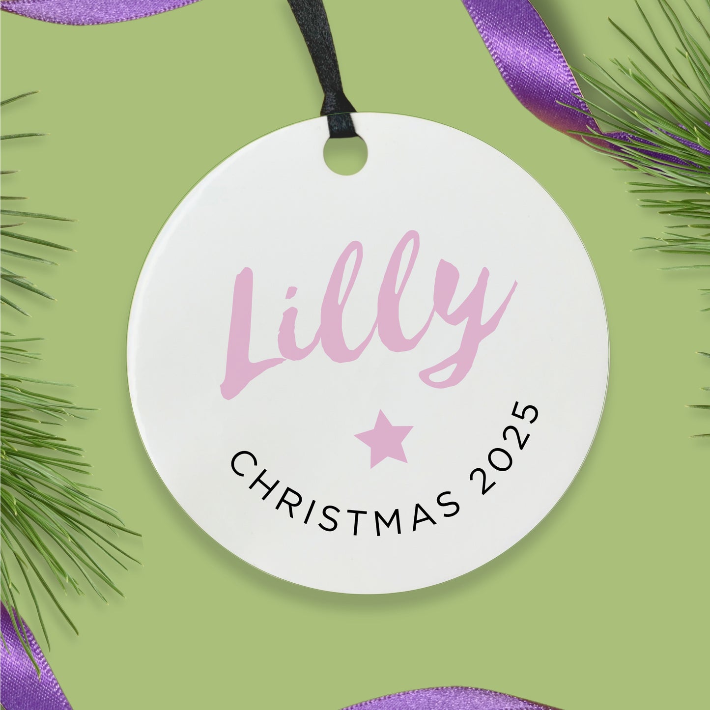 Round white ornament with custom name and Christmas 2025 text on a green background with purple ribbon and pine branches.