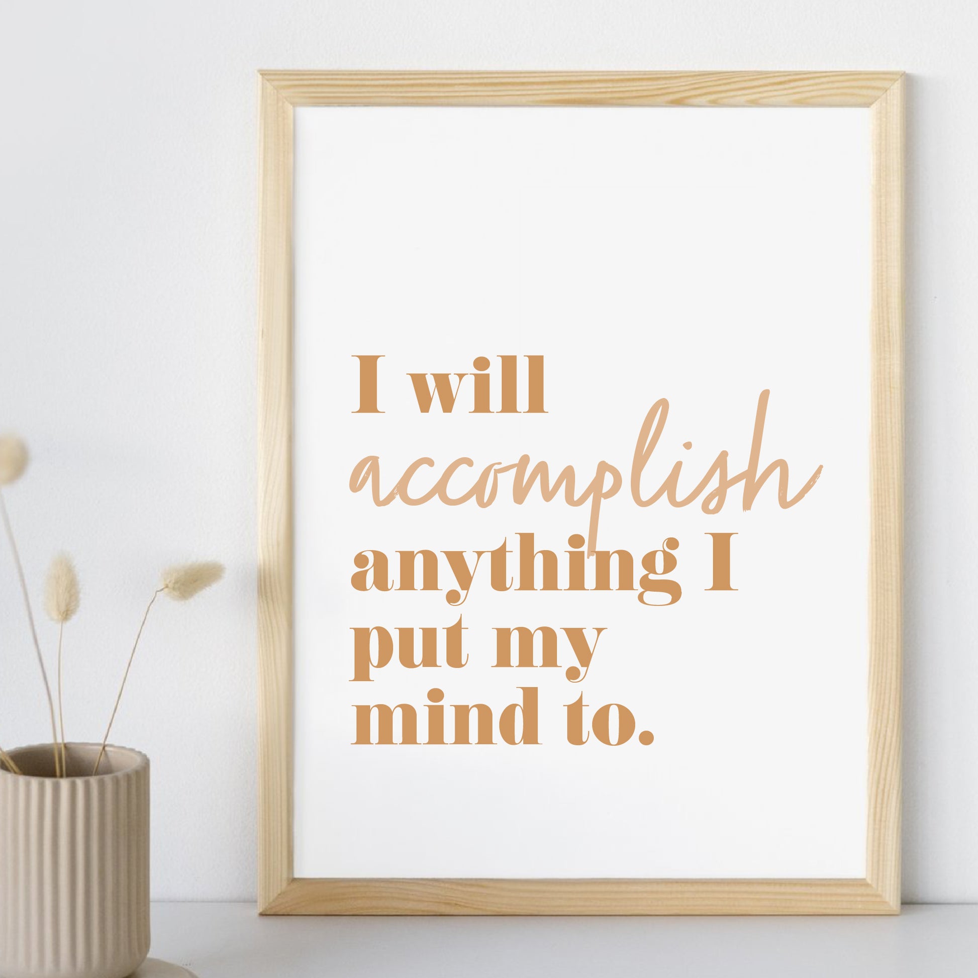 Framed motivational quote 'I will accomplish anything I put my mind to' on a white wall with a vase of dried plants.