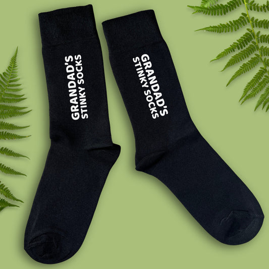 Black socks with 'Grandad's Stinky Socks' text on a green background with fern leaves.