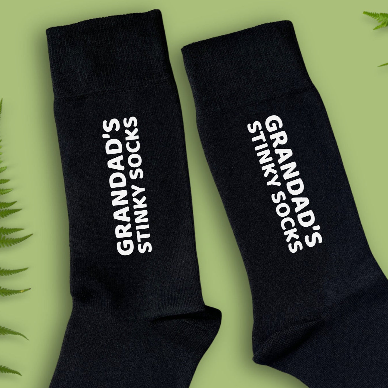 close up of black socks with 'Grandad's Stinky Socks' text on a green background with fern leaves.