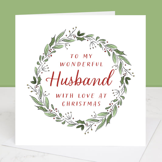 Greeting card with festive wreath design and text 'To my wonderful husband with love at Christmas' on a white background.