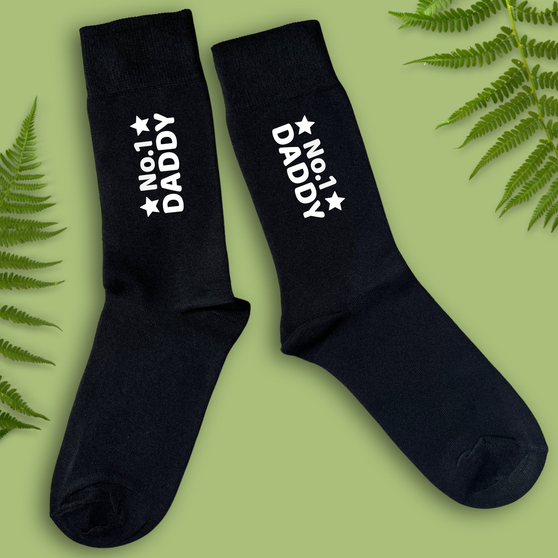 Black socks with 'No. 1 Daddy' text on a green background with fern leaves.